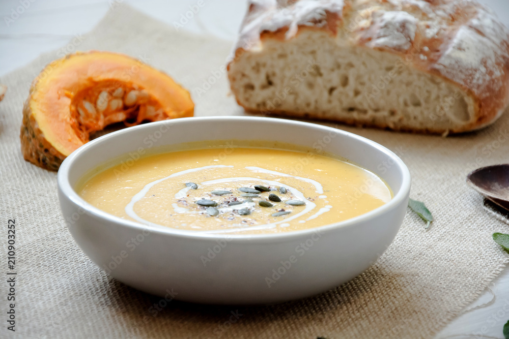 Pumpkin soup with pumpkin seeds. In white bowl, on hessian fabric. With pumpkin slice, wooden spoon and wholegrain rustic bread. Pumpkin soup with pumpkin seeds. In white bowl, on hessian fabric. With pumpkin slice, wooden spoon and wholegrain rustic bread.