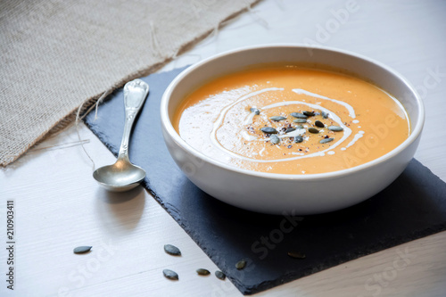 Pumpkin soup with pumpkin seeds. In white bowl, on slate board. With silver spoon and hessian fabric. 