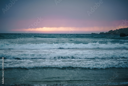 Beautiful pink and purple sunset on the beach. Sea with waves and foam in the evening.