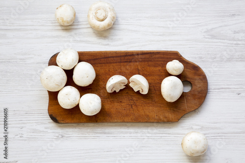 Champignon mushrooms on wooden board. White wooden background. From above.
