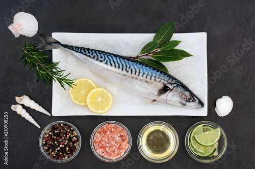 Mackerel fresh fish healthy heart food on crushed ice with bay leaf herb, peppercorns, olive oil, himalayan salt, lemon and lime on slate background. High in omega 3.