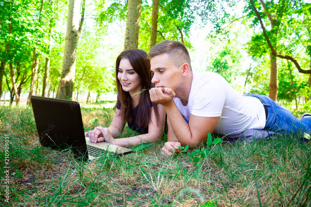 .guy with a girl lie on the grass in front of a laptop .guy with a girl lie on the grass in front of a laptop