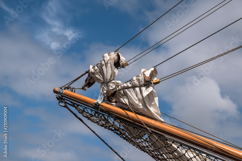 jib boom with reefed sails on the bow of a historic sailing ship against a blue sky with clouds, copy space photo