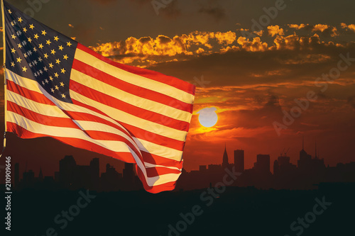 The American flag waving in View of Manhattan New York City sunset on the background