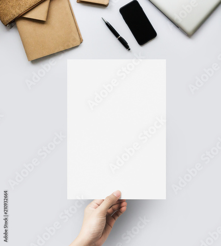 Hands holding blank paper sheet A4 size at table work space top view.