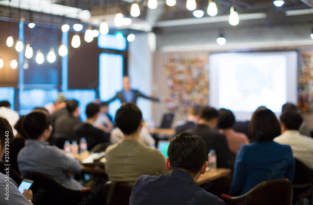 Presenter Presenting on Stage at Conference Meeting. Professional Lecture. Blurred De-focused Unidentifiable Presenter and Audience. Corporate Executive Manager Speaker. People Attendees