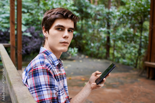 Man is sitting in the wooden pavilion and looking at the cellphone in the forest