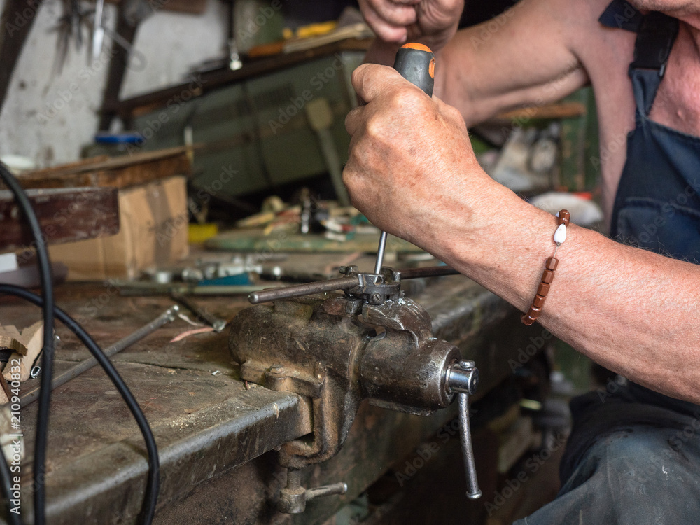 Older man sitting at workbench and working. Human's hands in process of screw cutting, close up view. Home workshop in harness. Hand tools on worktop. Blurred background, soft selective focus Older man sitting at workbench and working. Human's hands in process of screw cutting, close up view. Home workshop in harness. Hand tools on worktop. Blurred background, soft selective focus