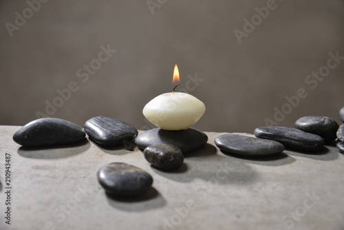 Candle with pile of black stones on gray background 