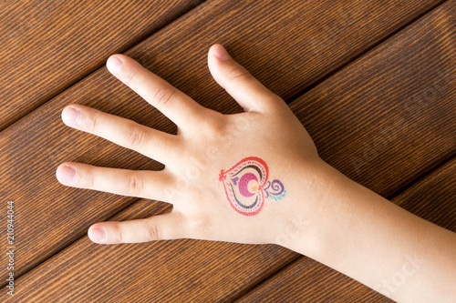 Hand of little girl with baby tattoo on wooden background.