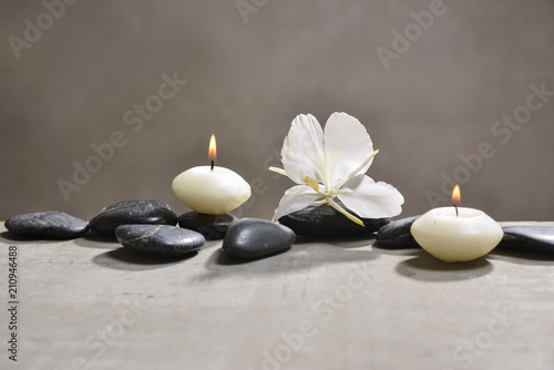 candle with pile of black stones and white orchid  on gray background