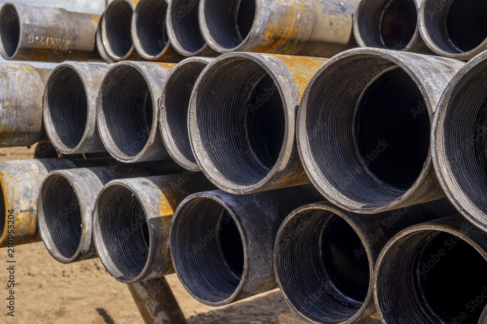 Oil Drill pipe. Rusty drill pipes were drilled in the well section. Downhole drilling rig. Laying the pipe on the deck. View of the shell of drill pipes laid in courtyard of the oil and gas warehouse. Oil Drill pipe. Rusty drill pipes were drilled in the well section. Downhole drilling rig. Laying the pipe on the deck. View of the shell of drill pipes laid in courtyard of the oil and gas warehouse.