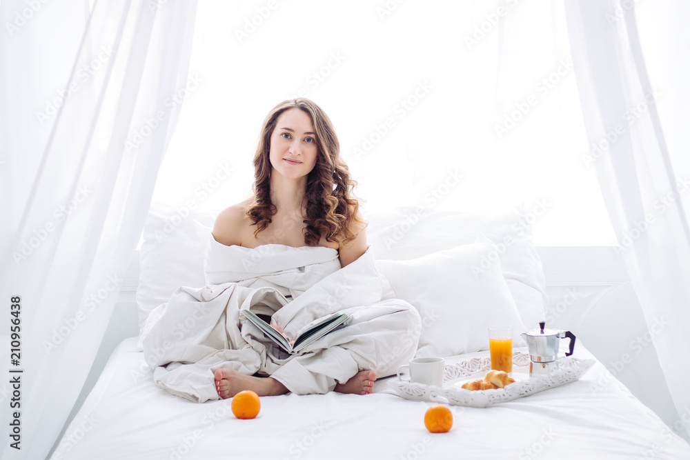 woman on the white bed, in blanket with book. healthy breakfast.
