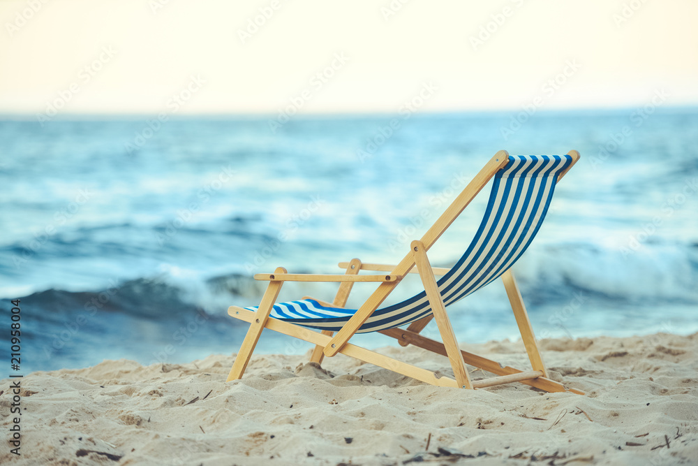 selective focus of wooden beach chair on sandy beach with sea on background