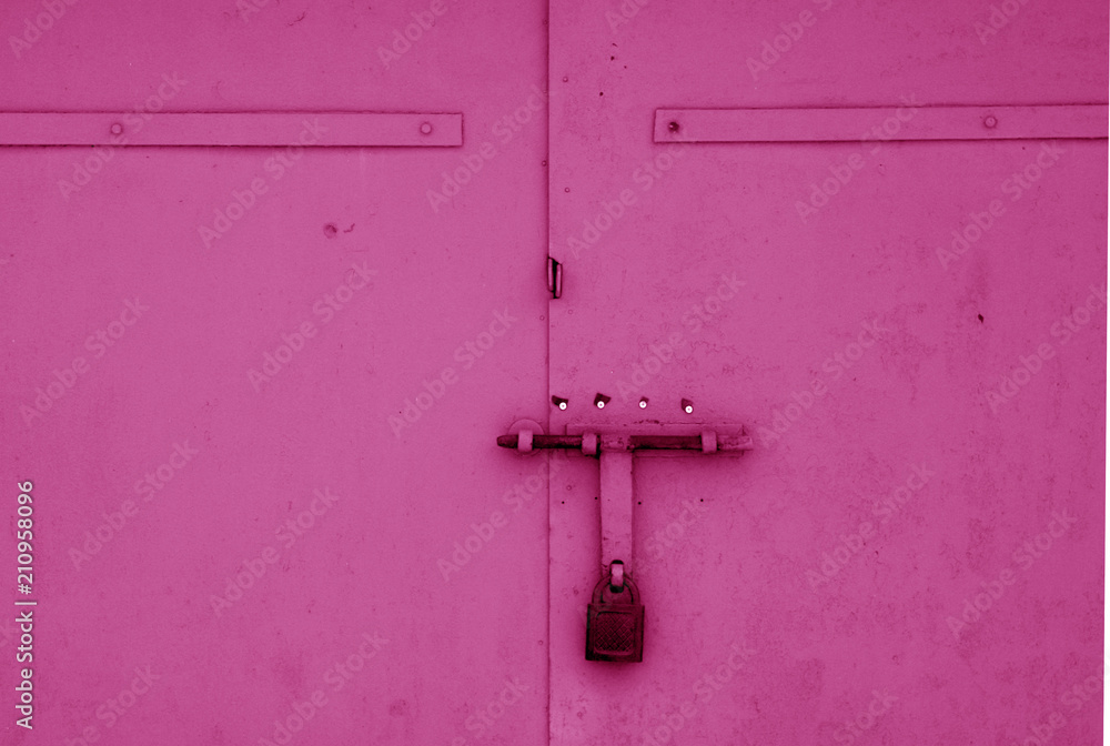 Old padlock on metal gate in pink color.