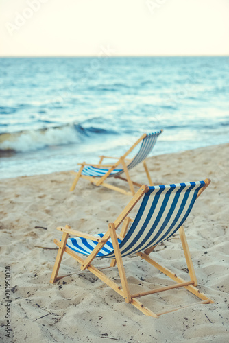 selective focus of wooden beach chairs on sandy beach with sea on background