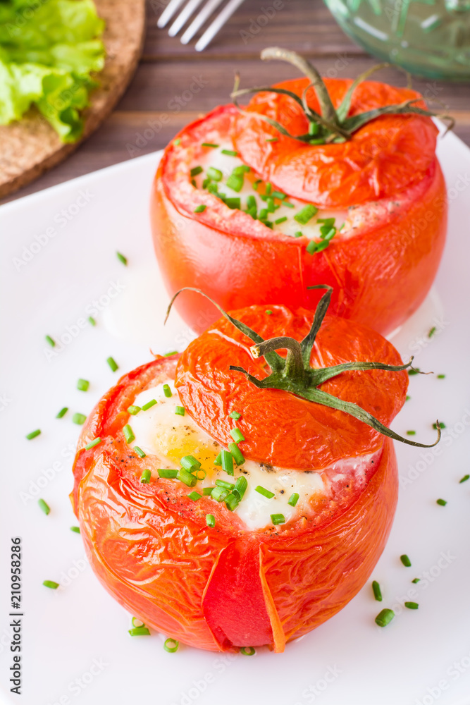 Close-up of fresh tomatoes baked with cheese and egg sprinkled with green onions on a plate on a wooden table Close-up of fresh tomatoes baked with cheese and egg sprinkled with green onions on a plate on a wooden table