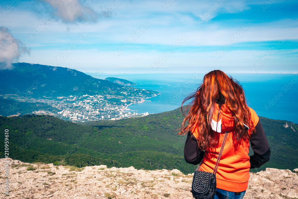 beautiful young woman with red hair on the mountain looks at the sea. Aerial panoramic view of the city of Yalta in Crimea, Russia.