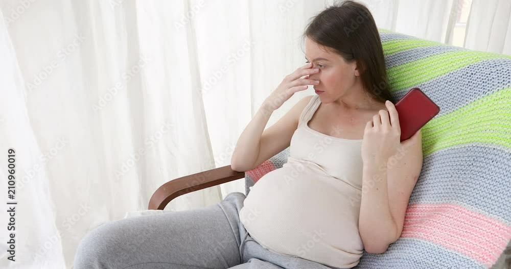 young pregnant woman sitting on sofa at home and having phone call looking sad young pregnant woman sitting on sofa at home and having phone call looking sad