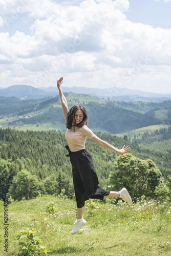 Cute girl is jumping against the backdrop of mountains and forests. Sunny summer day