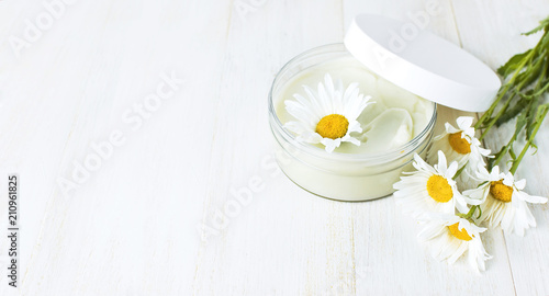 Opened plastic container with cream and chamomile flower on a light background. Herbal dermatology cosmetic hygienic cream Spa concept organic cosmetic Natural beauty product.