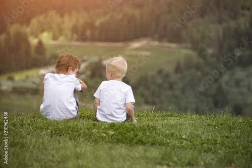 Two boys sit on the hill and talking cheerfully. Back view