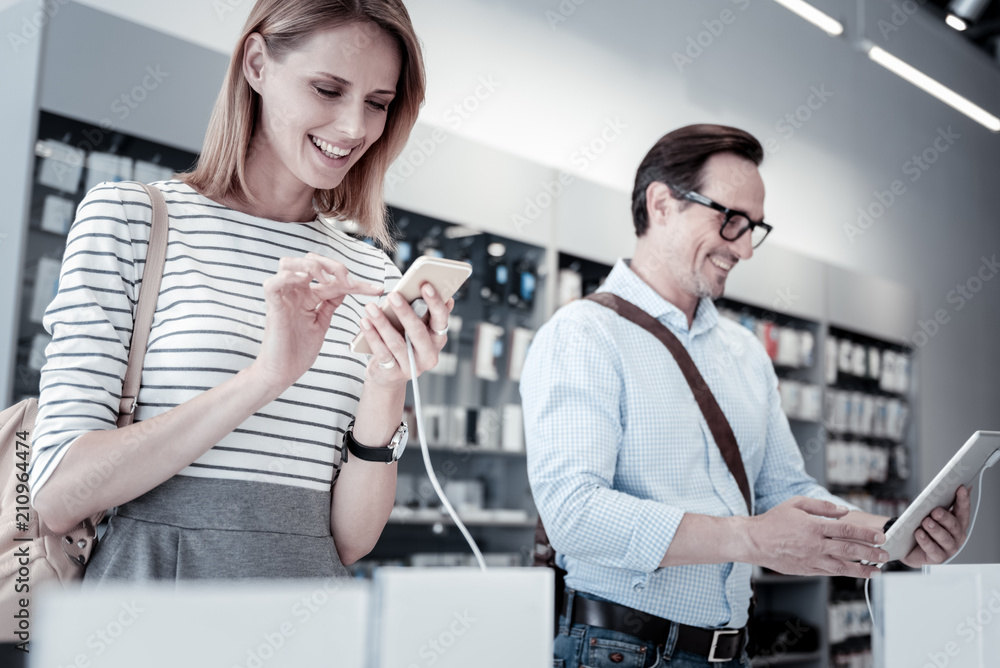 Different gadgets. Pleasant calm customers looking attentively at various devices in a new shop Different gadgets. Pleasant calm customers looking attentively at various devices in a new shop
