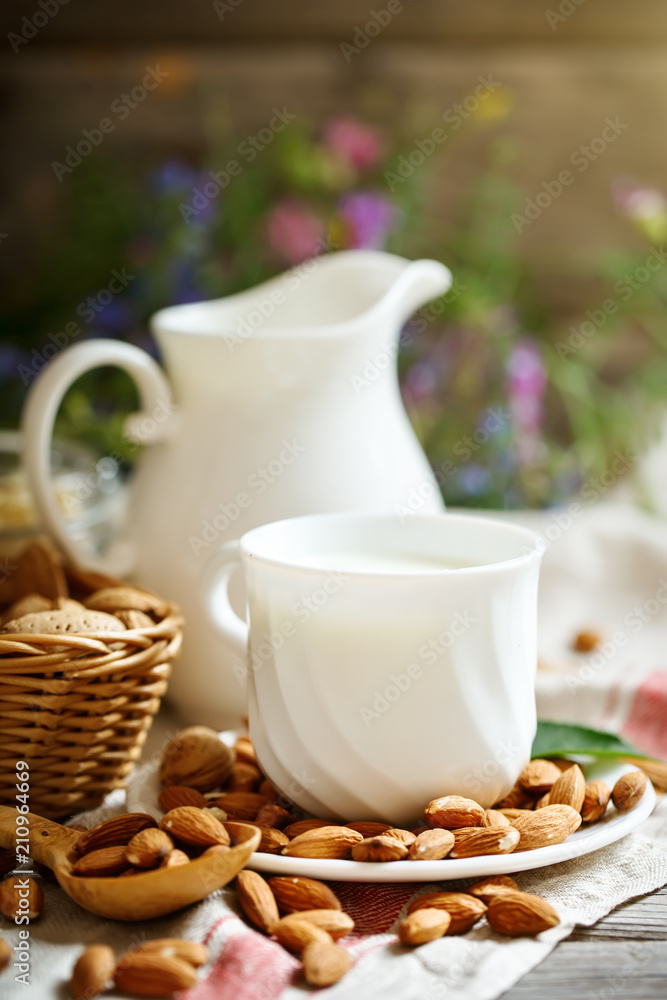 Fototapeta premium Almond and almond milk on a wooden table in the summer garden. Useful food.