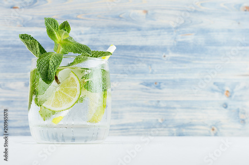 Refreshing transparent spring drink with slices lime, twig mint, ice, bubbled water, straw on soft blue wood plank, copy space, closeup.