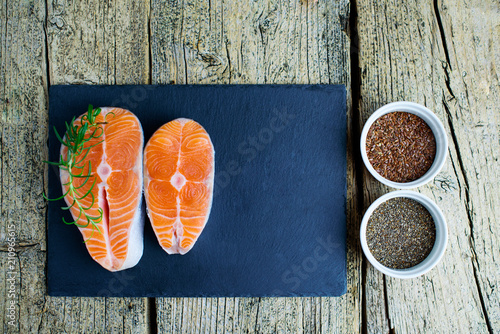 Two salmon steaks lie on a black board, and alongside there are vitamins and seeds of chia and flax. Top view. The choice to get vitamins