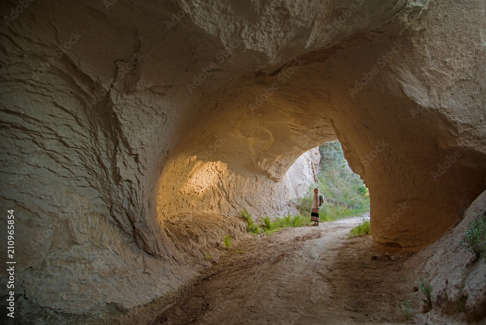 Naklejka premium Woman in sunlit natural rock tunnel