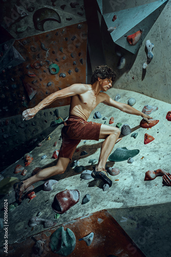 Free climber young man climbing artificial boulder indoors