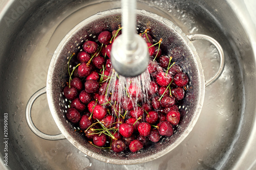 Slika na platnu Sweet cherry washing in metal colander in the kitchen sink.