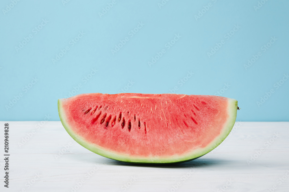 close up view of fresh watermelon slice on white surface on blue background close up view of fresh watermelon slice on white surface on blue background