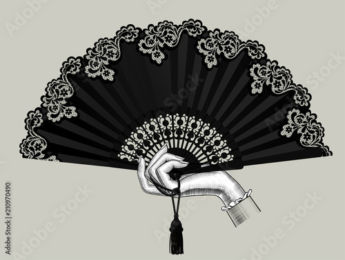 Female hand holding the black open fan with a tassel