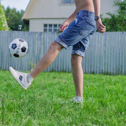 young man in denim jeans and white sneakers playing football ball outdoors. Amateur football player mint the ball