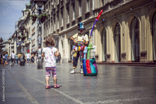 Little girl watching clown at the pedestrian street in the city