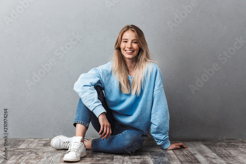 Happy young blonde girl sitting on a floor