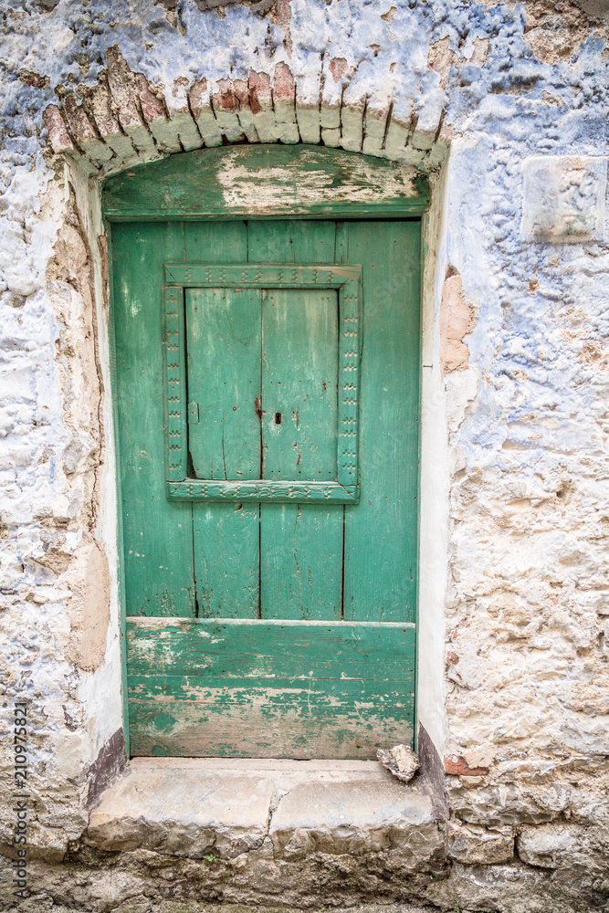 Old greenish blue wooden door and eroded wall. Front door.  Entrance to the house
