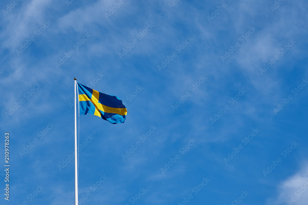 Flag of Sweden against a blue cloudy sky on a background. Copy space for text. Flag of Sweden against a blue cloudy sky on a background. Copy space for text.
