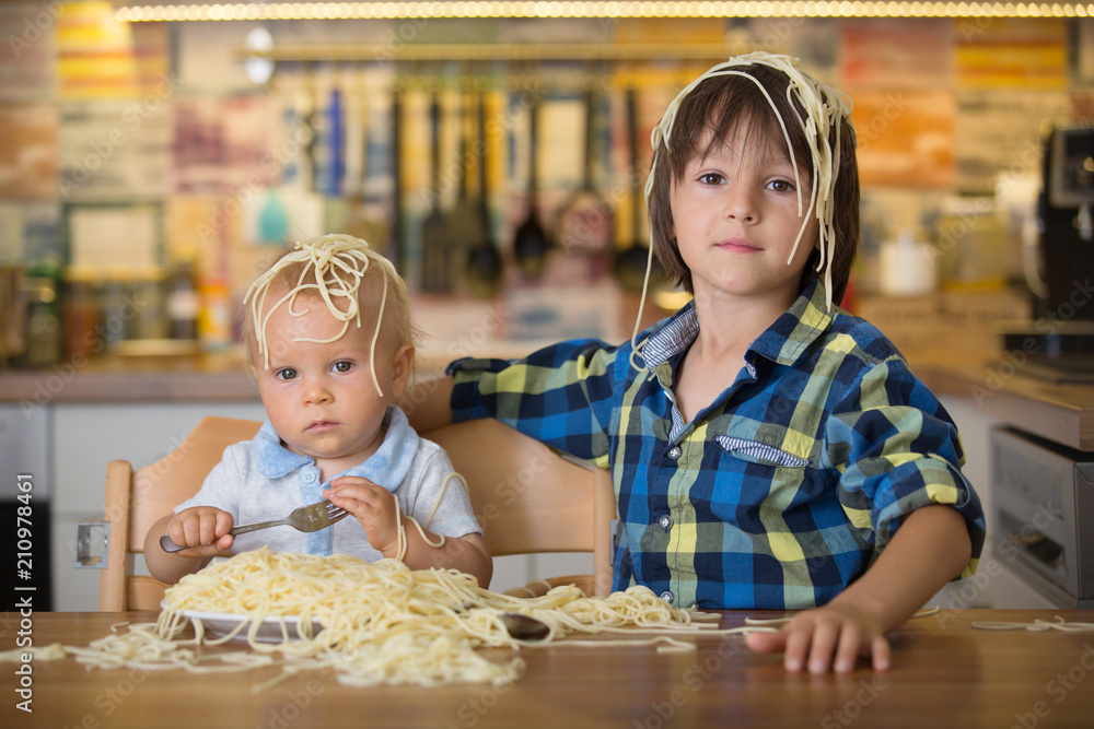 Little baby boy and his older brother, toddler child, eating spaghetti for lunch and making a mess Little baby boy and his older brother, toddler child, eating spaghetti for lunch and making a mess