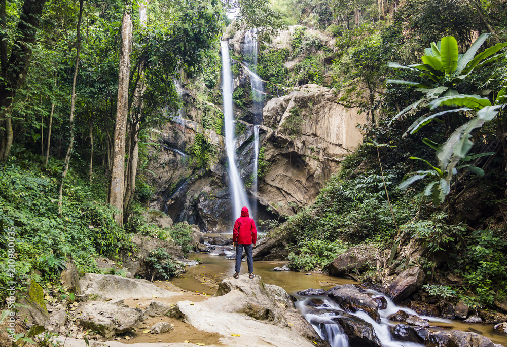 Naklejka premium man standing in forest near huge waterfall in jungle of thailand