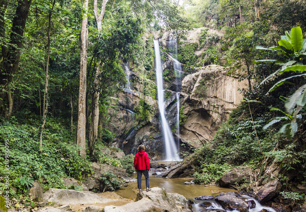 man standing in forest near huge waterfall in jungle of thailand man standing in forest near huge waterfall in jungle of thailand