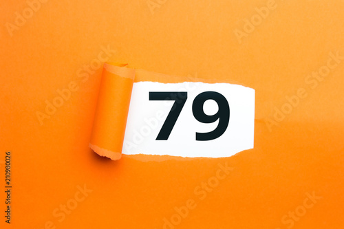 Zahl neunundsiebzig - 79 verdeckt unter aufgerissenem orangen Papier photo