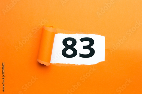 Zahl dreiundachtzig - 83 verdeckt unter aufgerissenem orangen Papier
