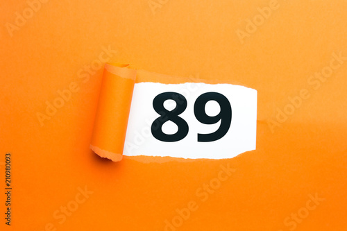 Zahl neunundachtzig - 89 verdeckt unter aufgerissenem orangen Papier photo