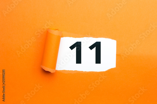 Zahl elf - 11 verdeckt unter aufgerissenem orangen Papier