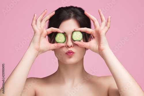 Young woman with cucumbers against eyes