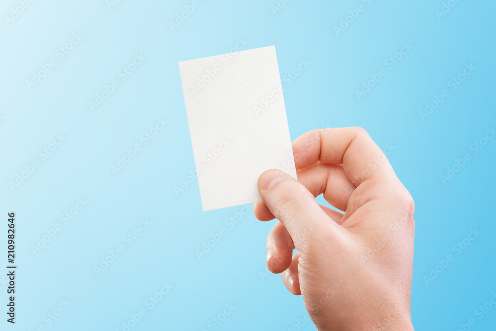 Male hand holding white business card at isolated blue background mockup. Male hand holding white business card at isolated blue background mockup.