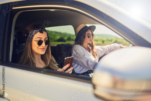Two girls driving in the car. One girl driving and other using smart phone for text message. © chika_milan